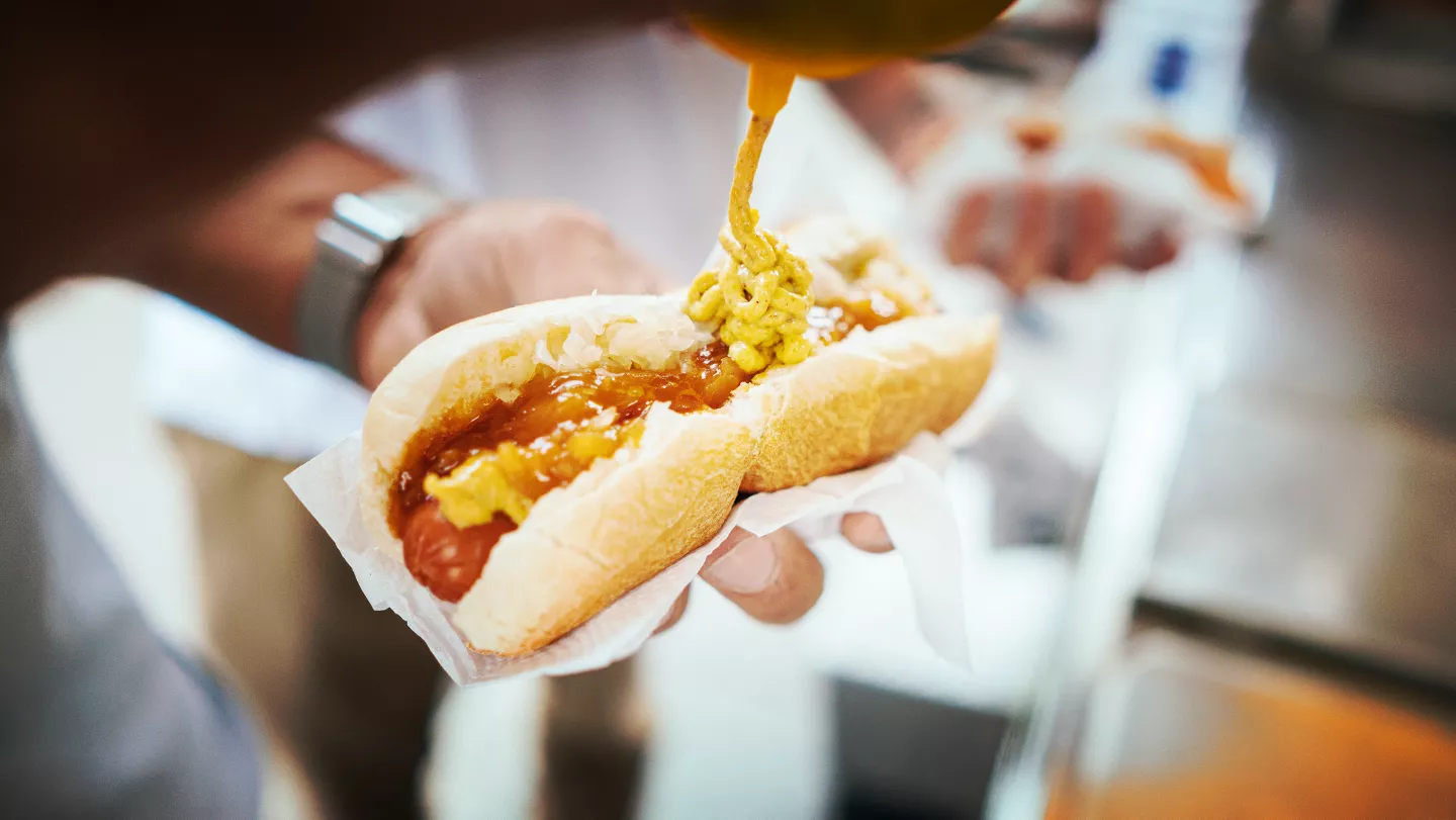Přidávání hořčice na domácí americký hot dog v chlebovém obalu.