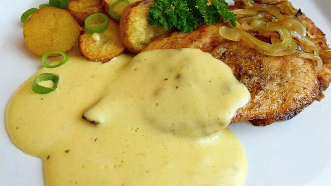 Pečené kuřecí steak s omáčkou, bramborami a cibulkou na talíři.