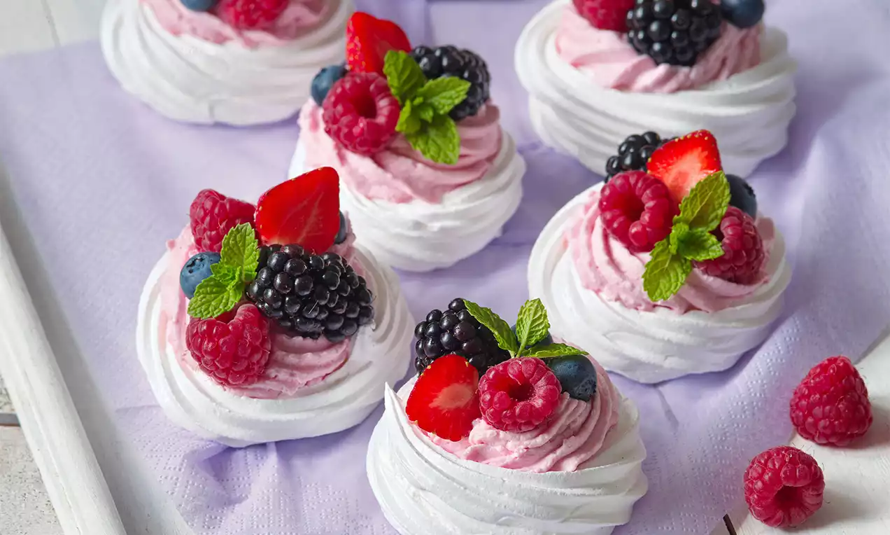 Mini dezerty Pavlova s ovocem na fialovém podkladu.