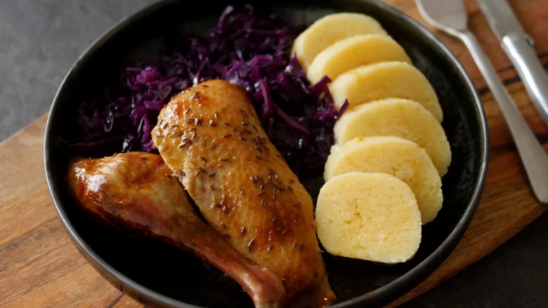 Pečená kachna se zelím a knedlíkem v černé misce.