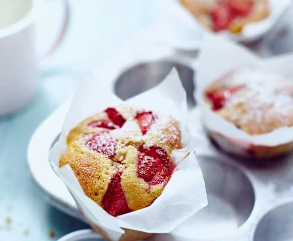 Svěží jahodové muffiny posypané cukrem pudrem v plechu.