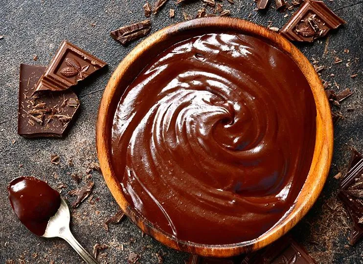 Čokoládová ganache v dřevěné misce s kousky čokolády.