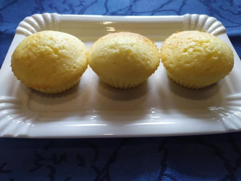 Tři žluté hrnkové muffiny na bílém podnose.