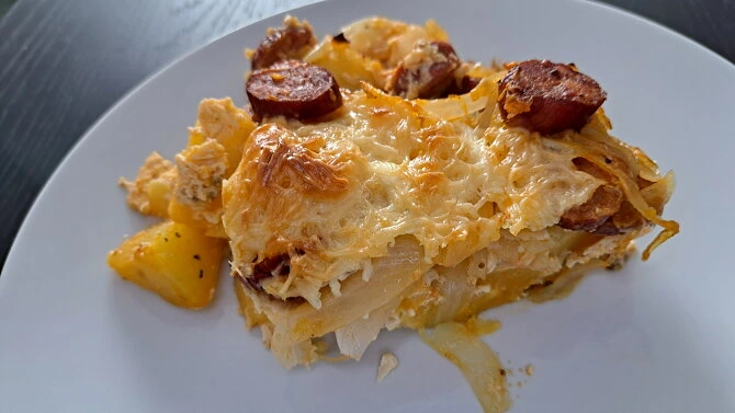 Zapečené brambory s klobásou na bílém talíři.