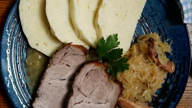 Překrojené vepřové maso s knedlíkem a zelím na talíři.