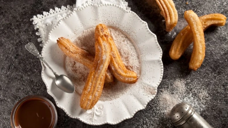 Zlaté churro posypané cukrem s čokoládovou omáčkou na tmavém podkladu.