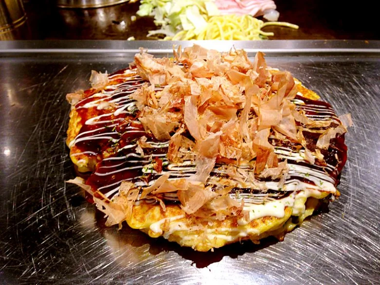 Okonomiyaki s kousky sušeného ryby na železném plechu.