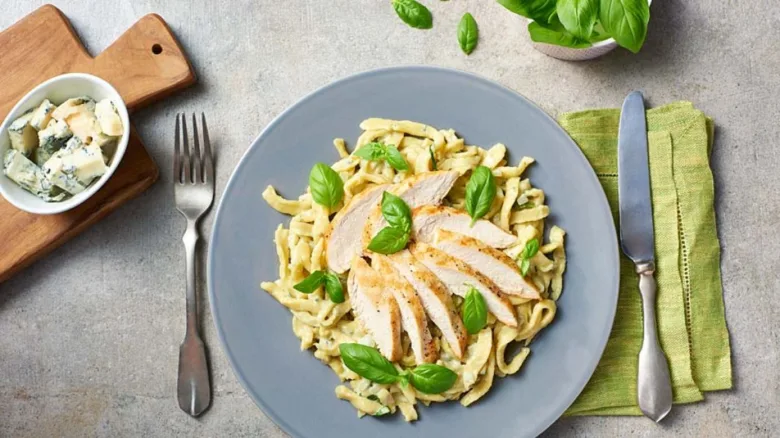Pasta s kuřecím masem v sýrové omáčce na talíři.