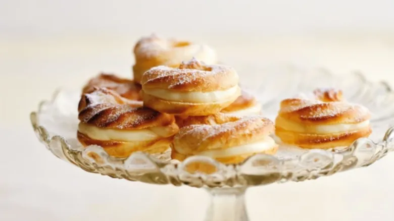 Zlaté krémové donuty na skleněném podstavci posypané cukrem.
