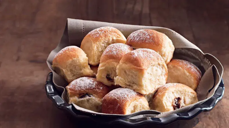 Kosár s čerstvými buchty z povidl posypaný cukrem pudrovým.