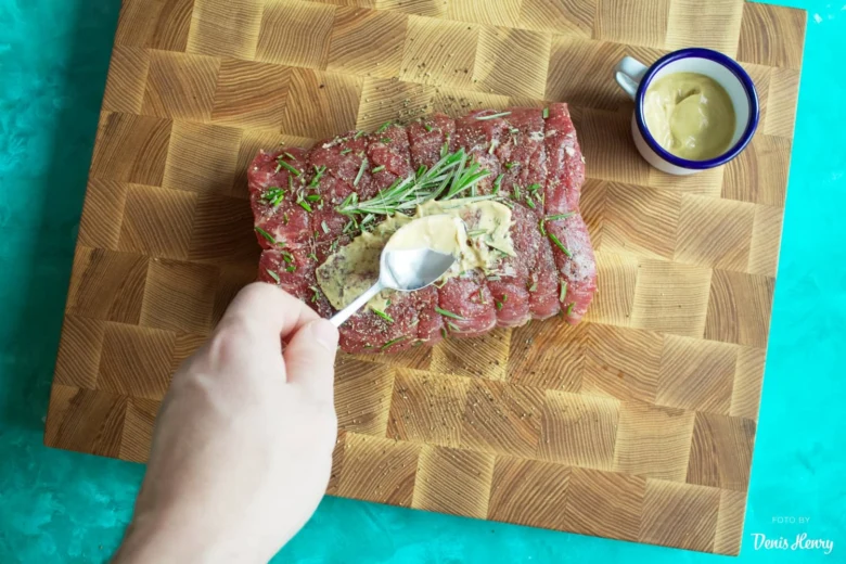 Ruka mazá hořčici na syrové hovězí maso s bylinkami.