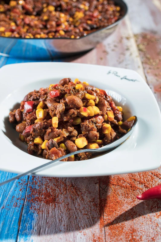 Kousek chilli con carne s fazolíky a kukuricí v bílé misce.