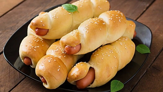 Zlatohnědé páreky v rohlíku s sezamem na talíři.