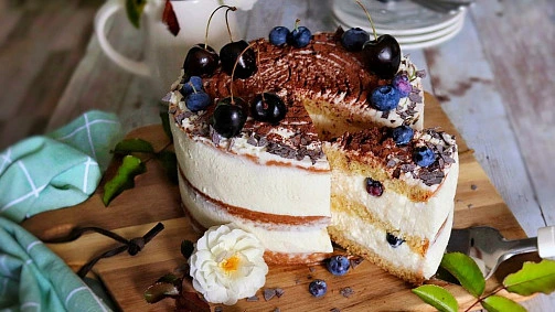 Složený dort s mascarpone, ovocem a čokoládou na dřevěném podnosu.