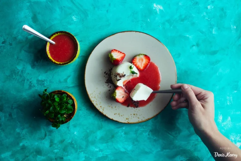 Panna cotta s jahodami a ovocnou omáčkou na talíři.