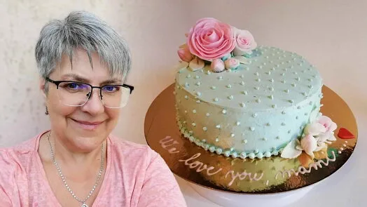 Žena stojí vedle ozdobeného dortu s květinami na zlatém podstavci.