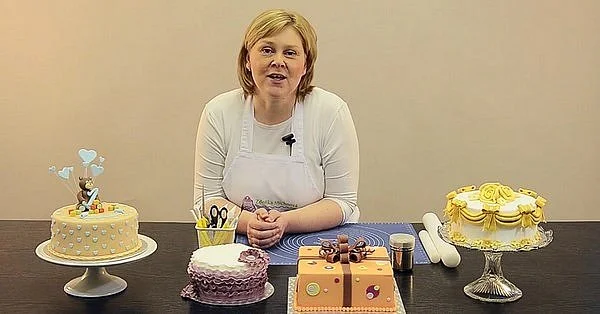 Žena s různě zdobenými dorty a náčiním na stole.