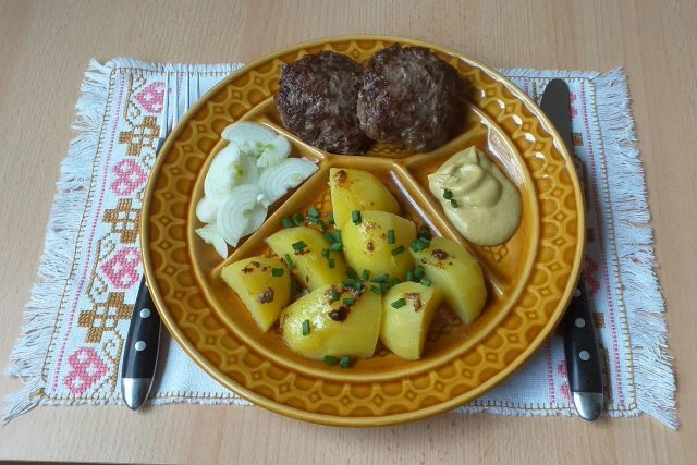 Biftečky z mletého masa s bramborami na žlutém talíři.