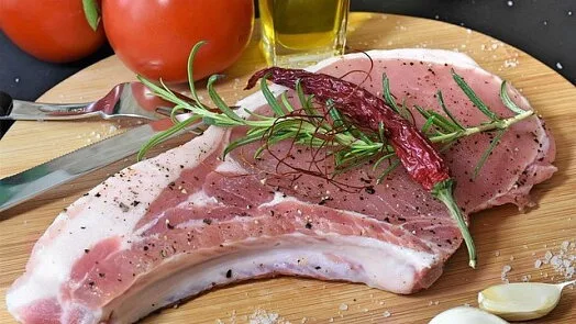Surová vepřová plec s rozmarýnem a kořením na dřevěném talíři.