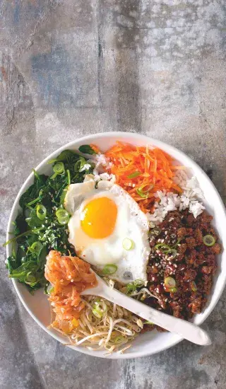 Bibimbap s vejcem na slupku a zeleninou v bílé misce.