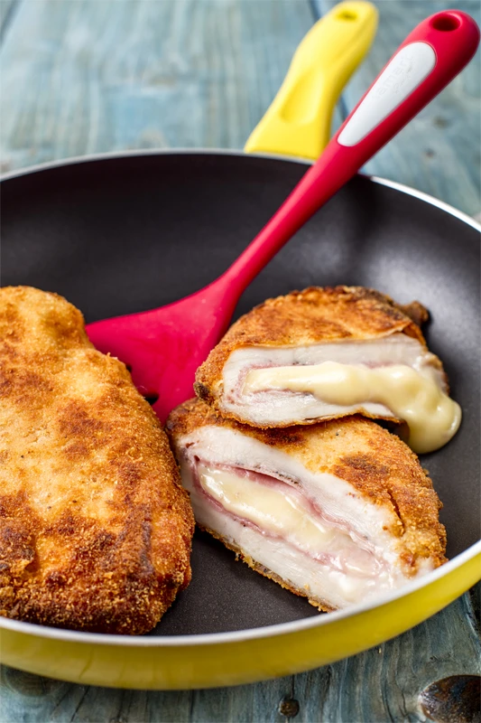 Zlatě opečené kuřecí cordon bleu s taveným sýrem v pánvi.