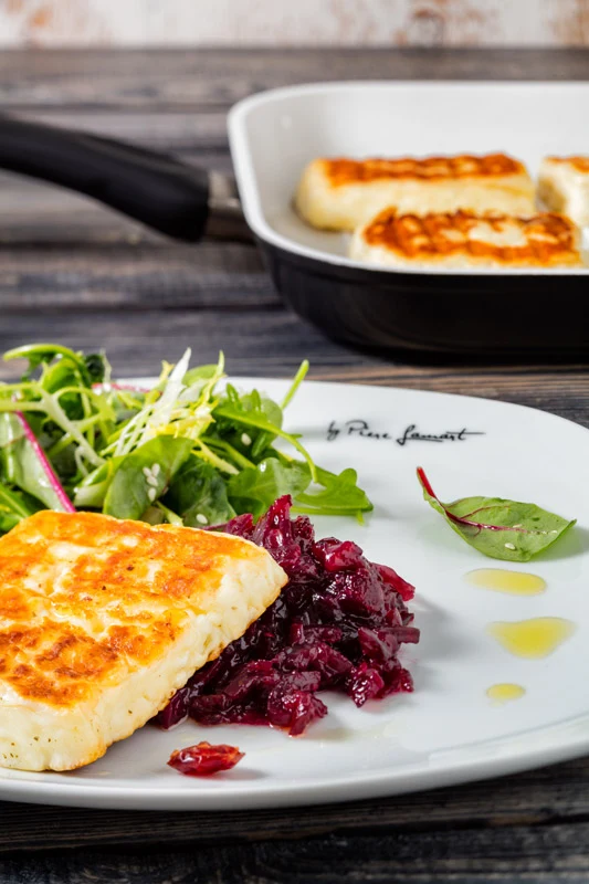 Grilovaný sýr halloumi podávaný se salát a červeným křovím na bílém talíři.