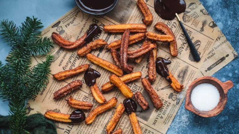 Zlaté churros s čokoládovou omáčkou na starém papíru.
