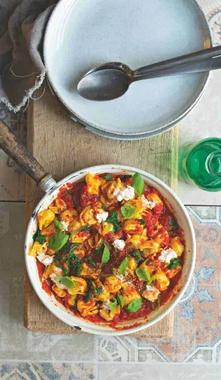 Tortellini v omáčce s nivou a bazalkou na dřevěném podstavci.