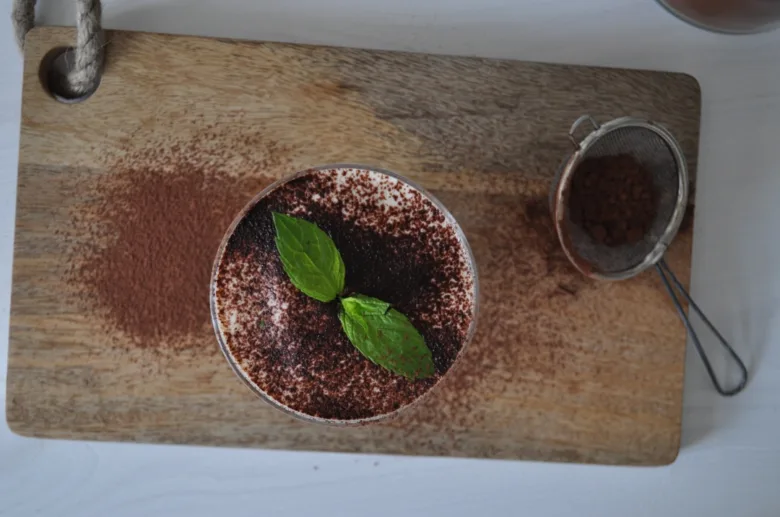 Hotový pudink Tiramisu posypaný kakaem na dřevěném prknu.