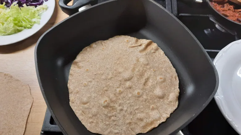 Pekoucí domácí tortila v pánvi s přílohami.