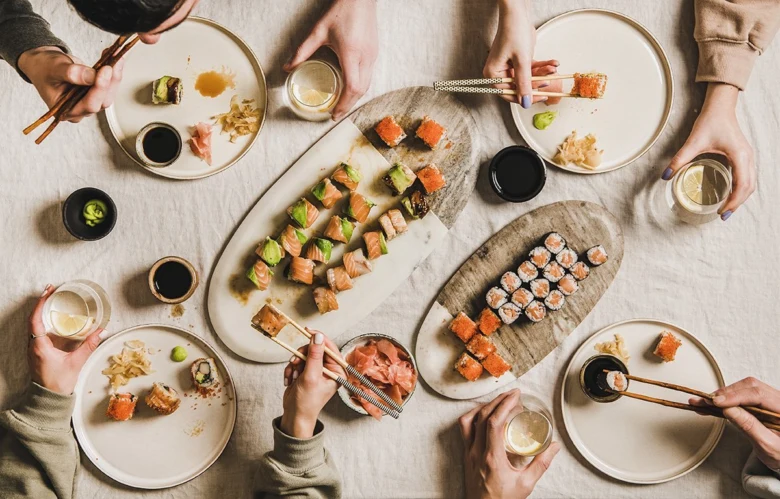 Lidé sdílejí sushiové rolky na dřevěných deskách kolem stolu.