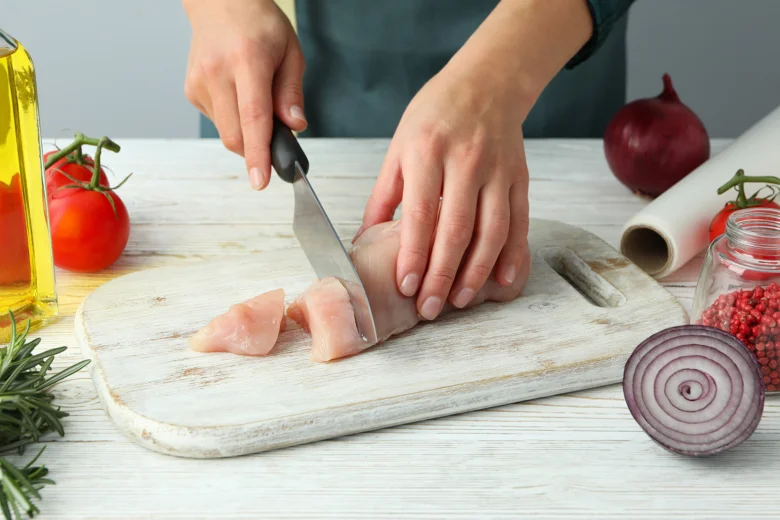 Rezařka krájí kuře na prsíčka s čerstvými ingrediencemi.