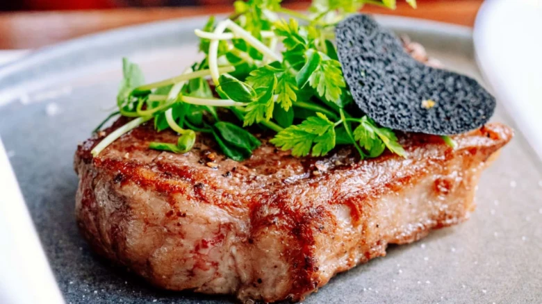 Připravený steak na pánvi s čerstvou bylinkou.
