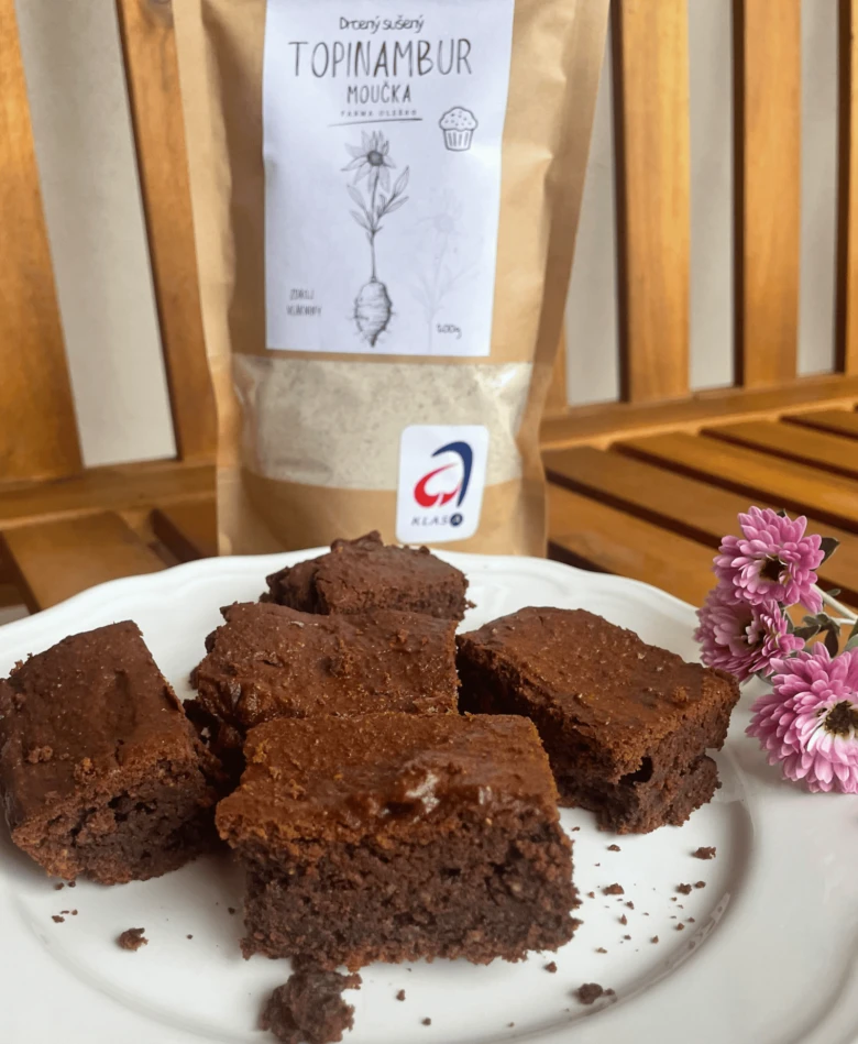 Domácí čokoládové brownie z moučky topinamburu na bílém talíři s balením v pozadí.