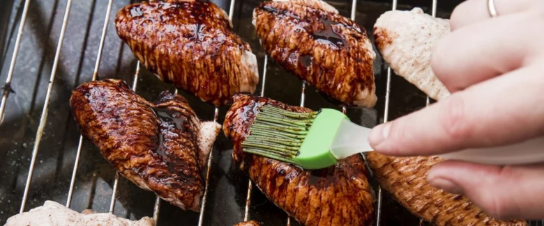 Ruce natírají pečené kuřecí křídla zelenou bbq omáčkou na grilu.