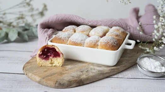Kynuté knedlíky s jahodovou náplní v bílé misce posypané cukrem.