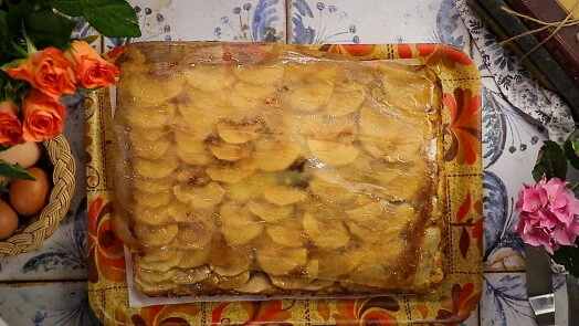 Hotový obrácený jablečný koláč na podnosu s květinami.