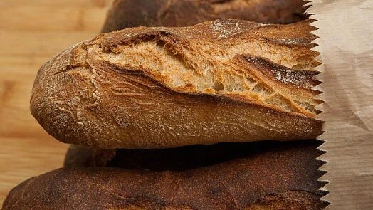 Zlatohnědá houska s křupavou kůrkou v hnědém papírovém obalu.