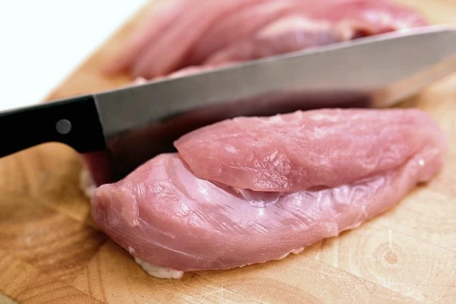 Surový vepřový řízek se řeže na dřevěném prknu.