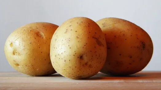 Tři celá žlutá brambory na dřevěném povrchu.