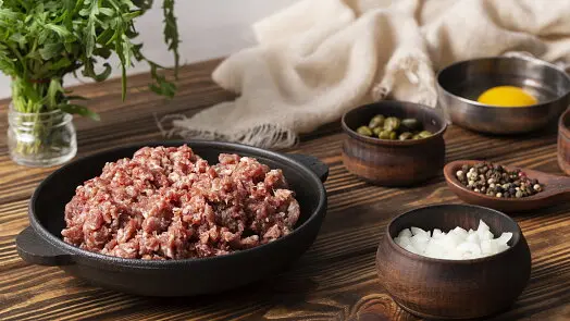 Surová mleté maso s ingrediencemi pro pomazánky na dřevěném stole.