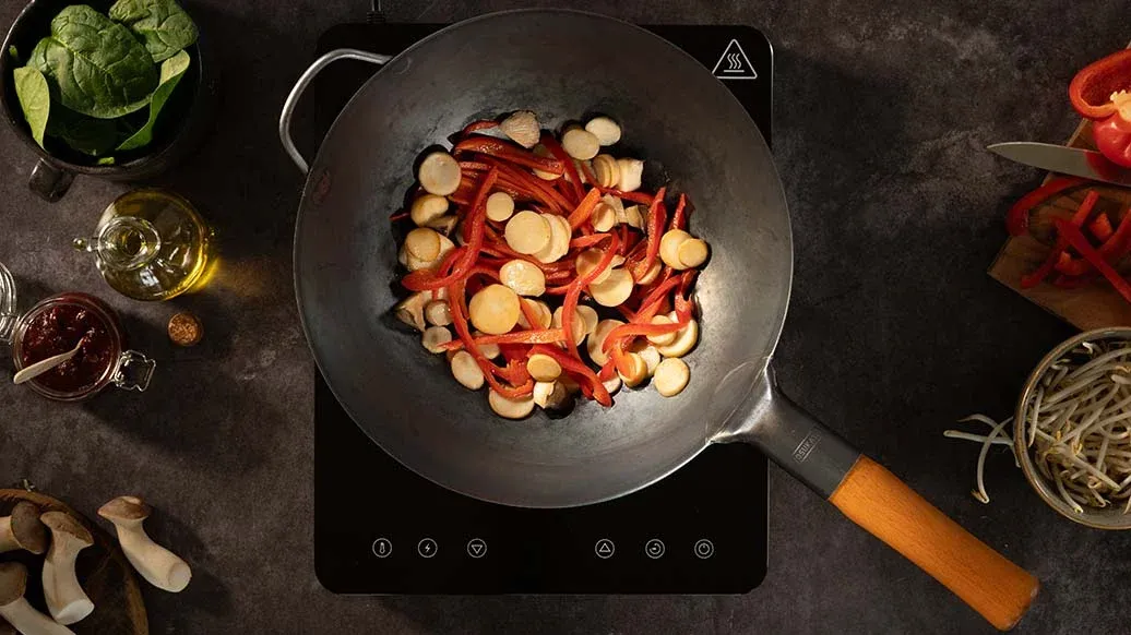 Wok s vařenými zeleninovými ingrediencemi na indukční varné ploše.
