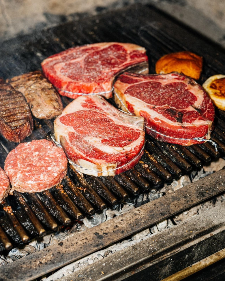 Surové steak na roštu nad uhlím při grilování.