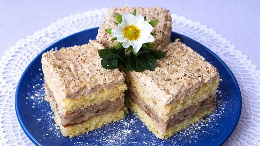 Tři řezy s vrstvami krému a strouhankou na modré talíři.