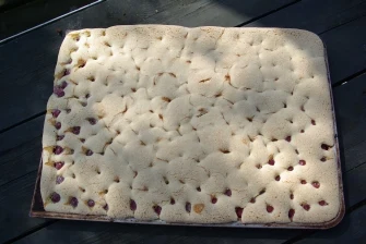 Hotovo piškotová bublanina s ovocem na tmavém dřevěném stole.