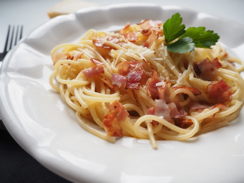 Připravená spagetti karbonara s kousky slaniny na bílém talíři.