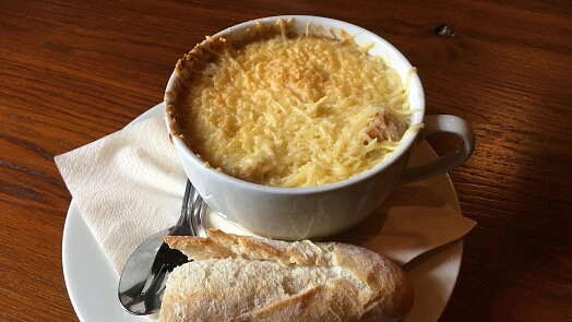 Miska cibulačky s roztopeným sýrem a kouskem chleba.