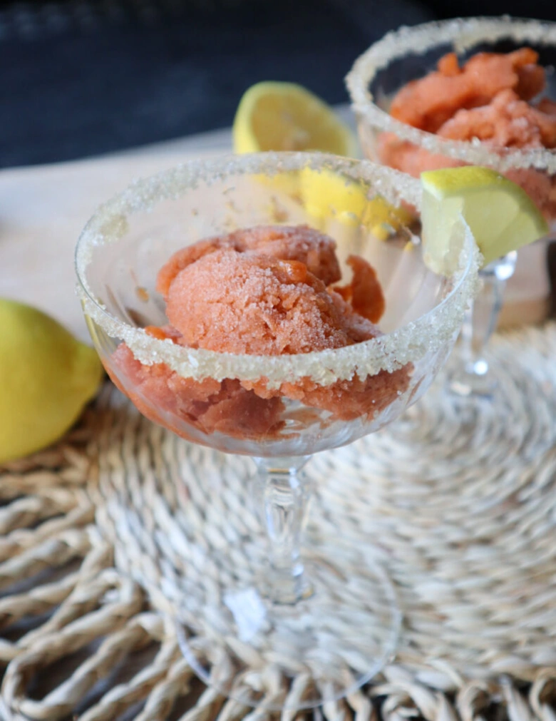 Růžové sorbet v sklenici s cukrem na okraji a citronem.