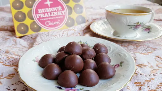 Pralinky s rým v krabičce na talíři vedle šálku čaje.