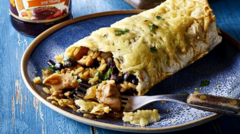 Půlkrájovaný burrito s rýží, fazolí a kuřecím masem na talíři.